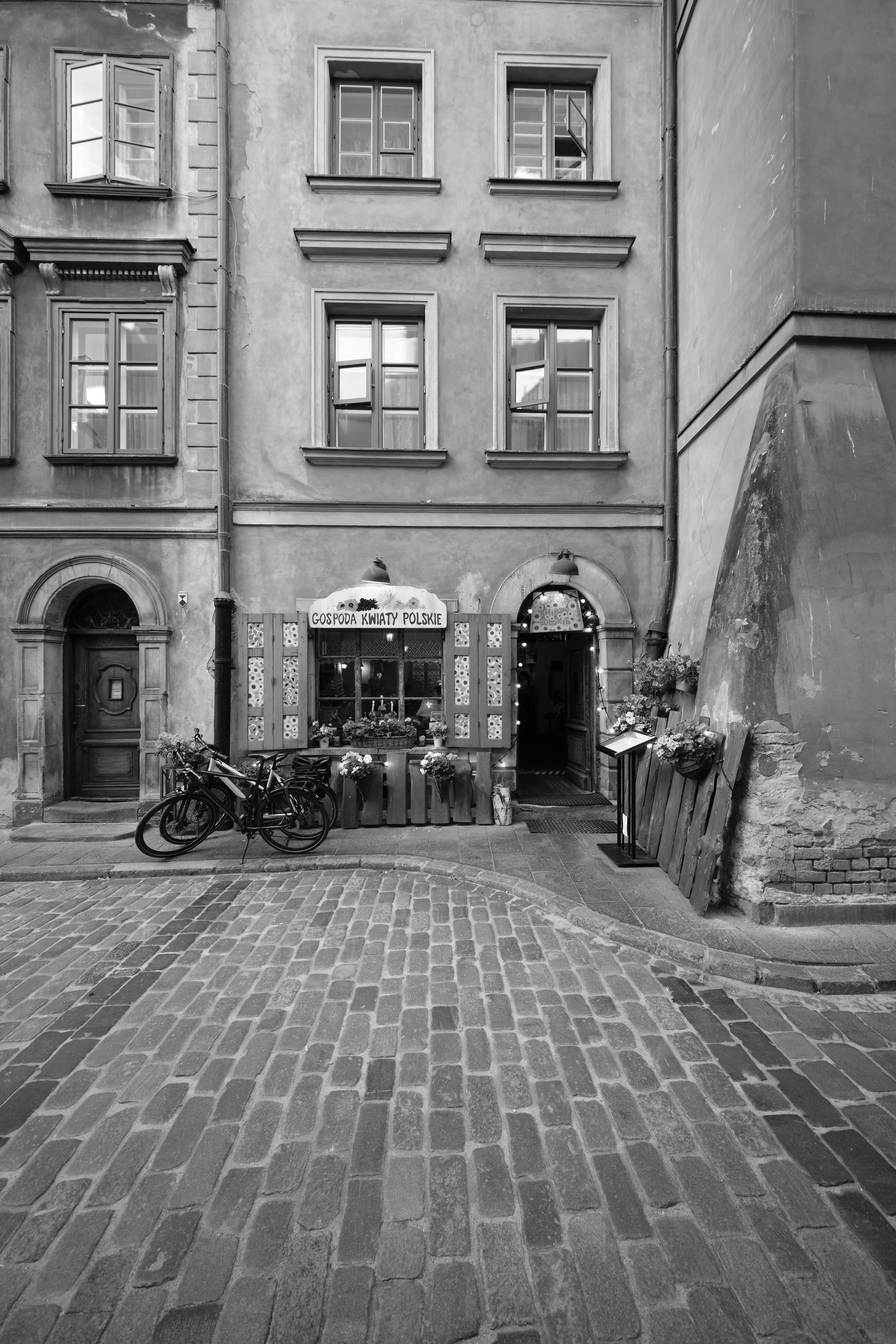 Schwarzweisses Altstadtgebaeude mit Laden, Fahrrad und Kopfsteinpflasterplatz