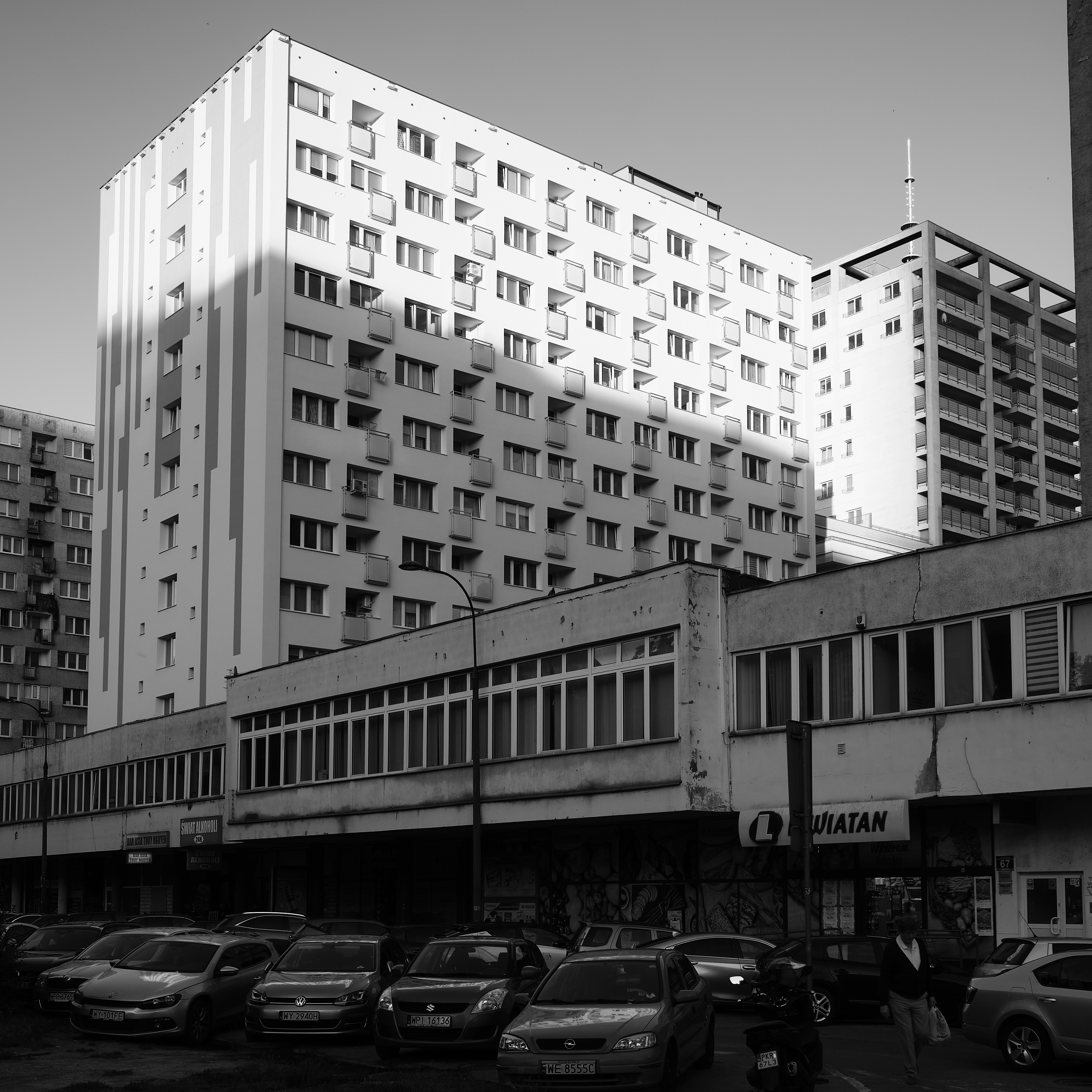 Weiße Hochhäuser mit Schattenwurf hinter grauem Flachbau und Autos