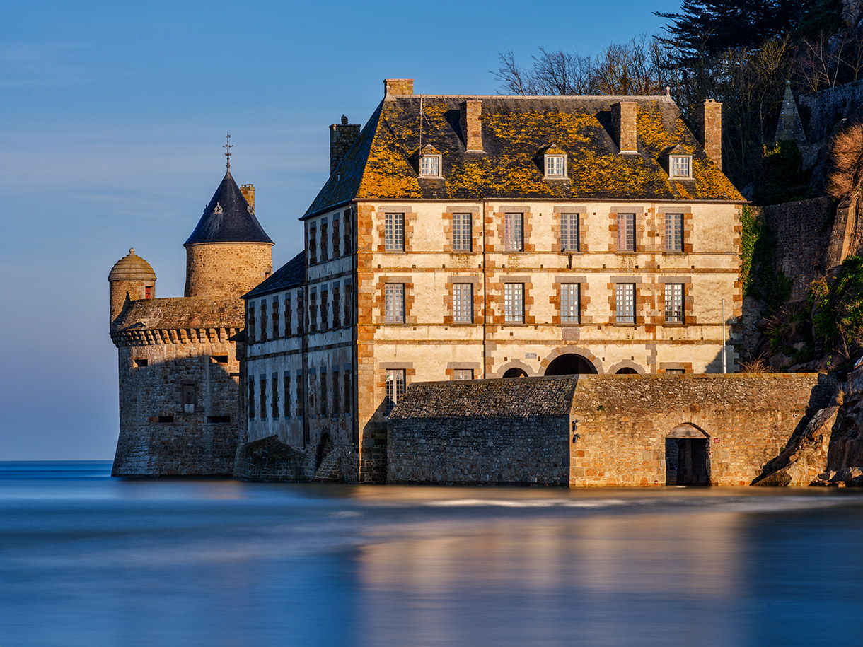 Historisches Steingebaeude mit Turm am ruhigen Wasser im warmen Abendlicht