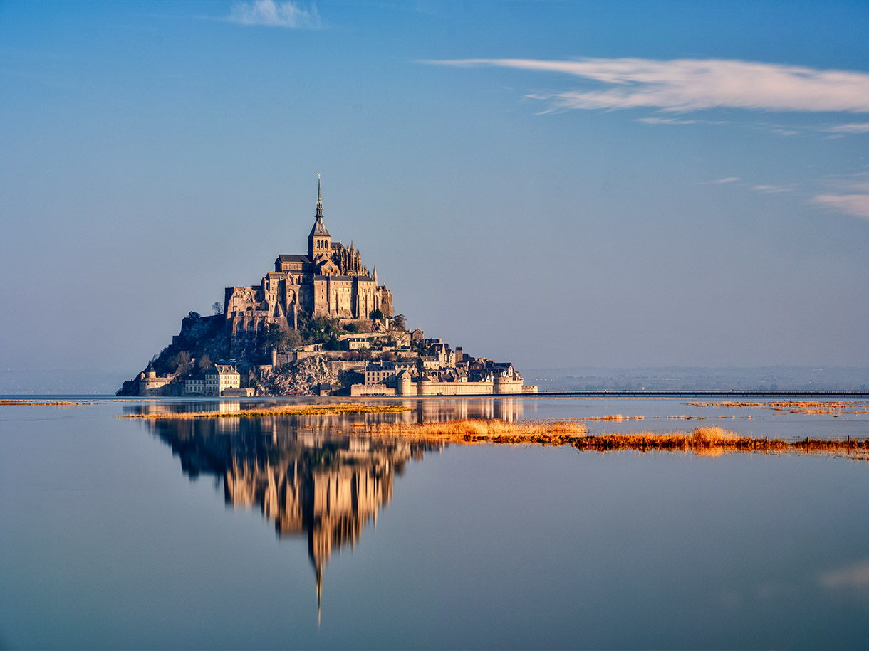 Der Mont Saint Michel spiegelt sich majestaetisch im ruhigen blauen Wasser